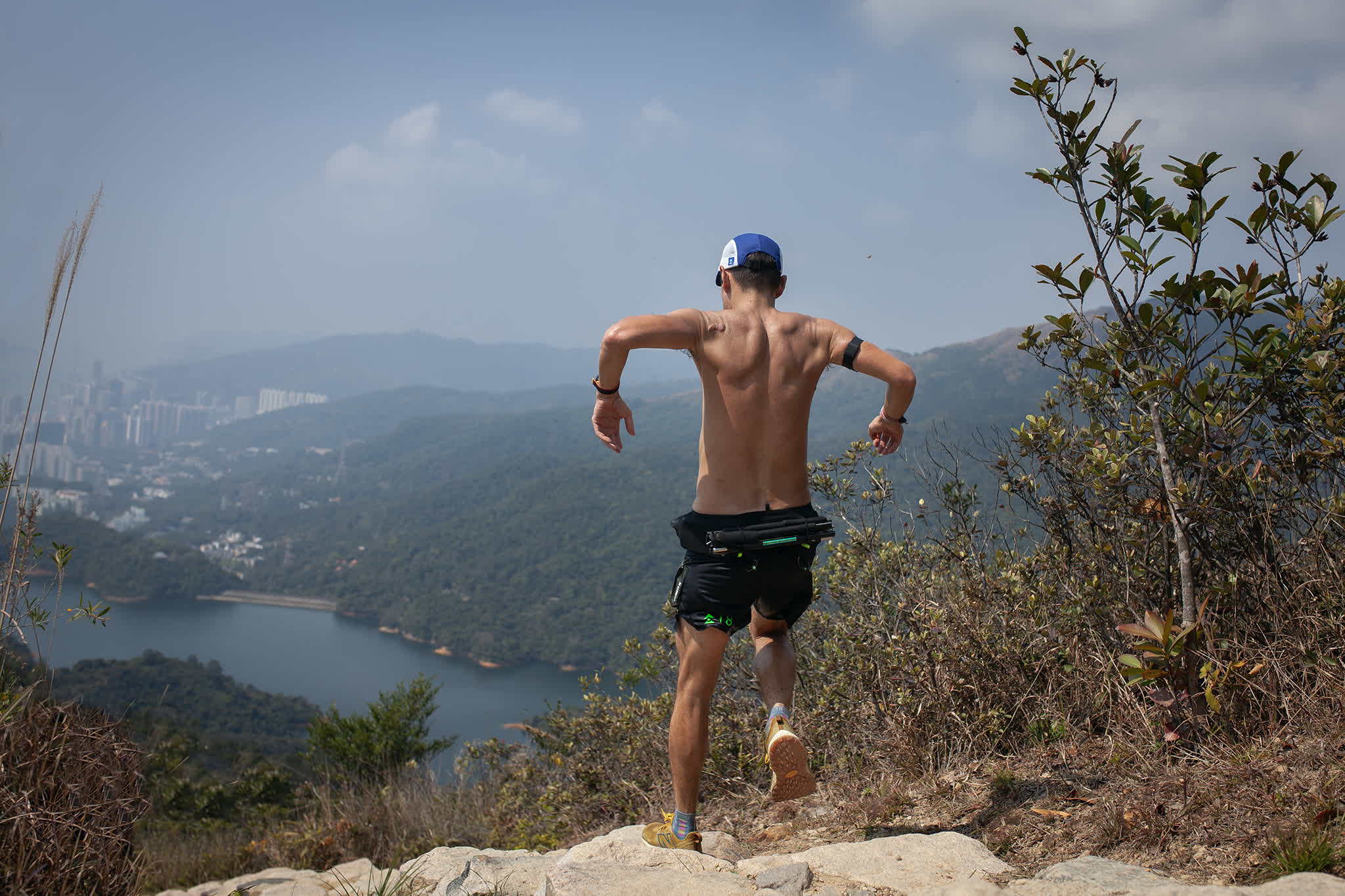 A runner cresting a ridge above a reservoir, the city beyond